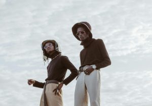 Stylish young men in modern outfits posing outdoors under cloudy sky.