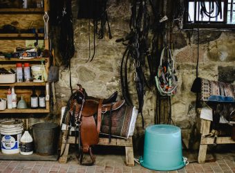 A cozy stable with equestrian equipment, including saddles and pails, against a stone wall.